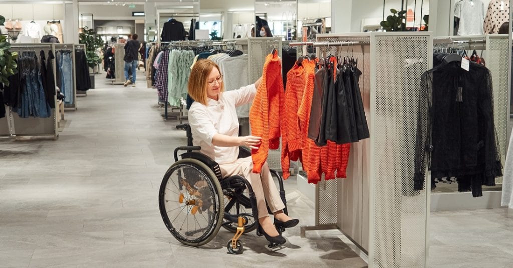 Frau im Rollstuhl kauft barrierefrei im Modegeschäft ein